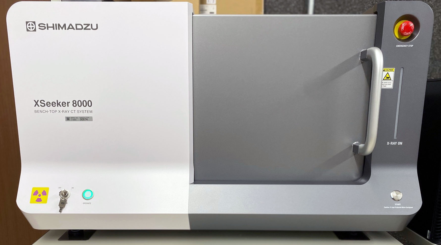 Shimadzu XSeeker 8000 bench-top X-ray CT system with a gray front access door and emergency stop button.