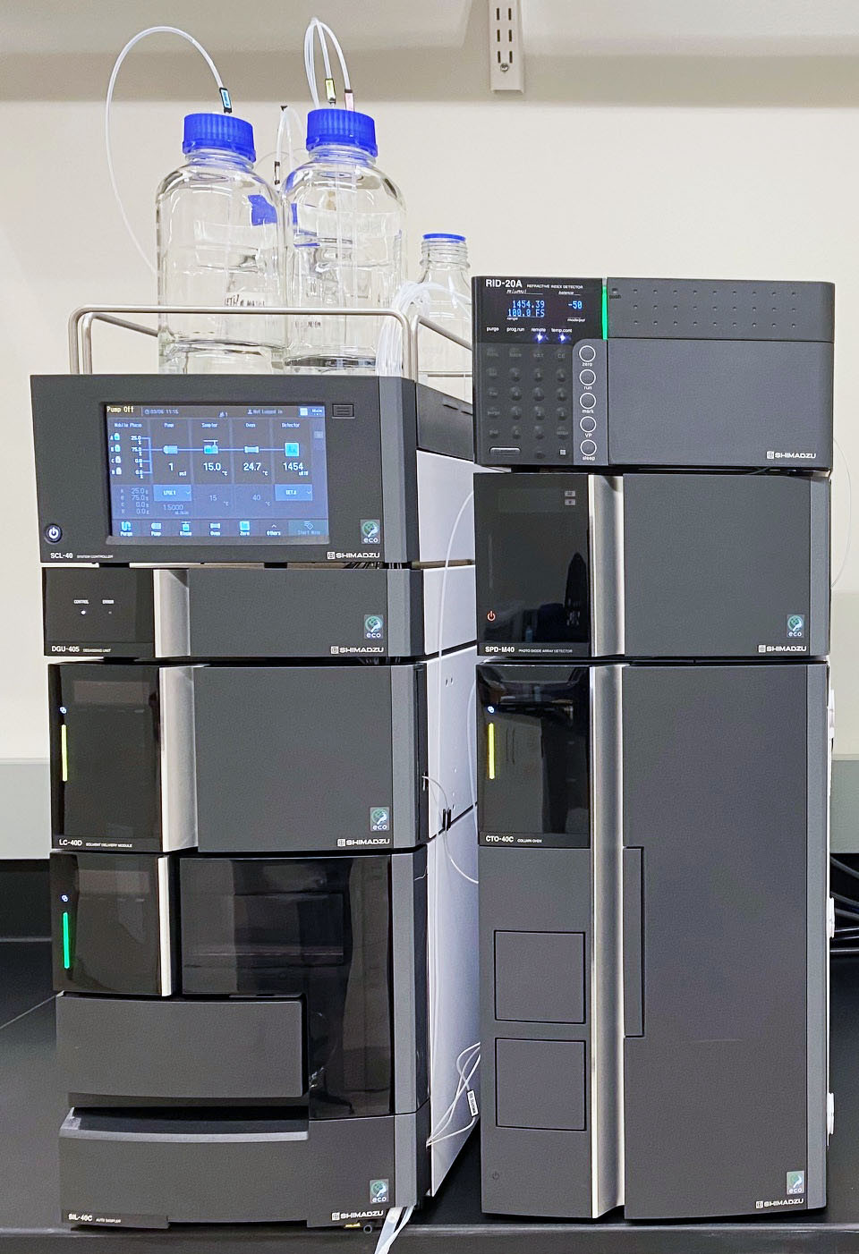Shimadzu HPLC system with solvent bottles, stacked control modules, detectors, autosampler, and column oven.